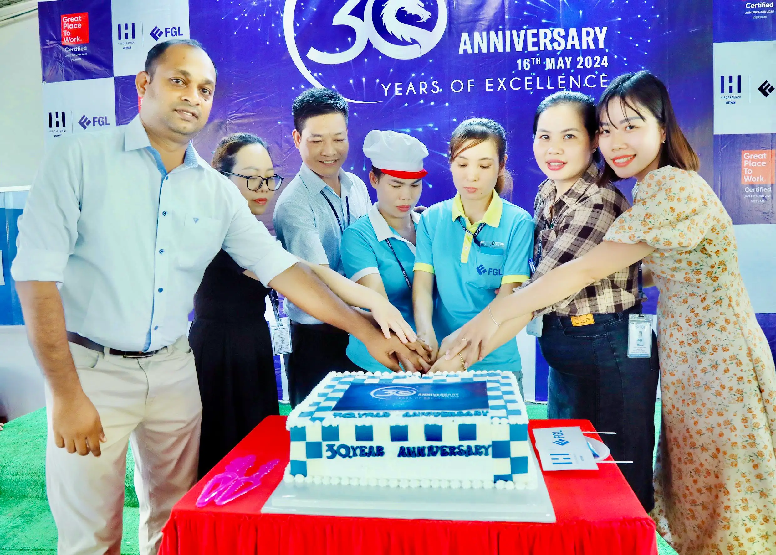 Employees holding hands on top of the anniversary cake